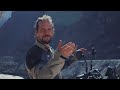 A person gestures near a Himlayan 450 motorcycle in a mountainous landscape.