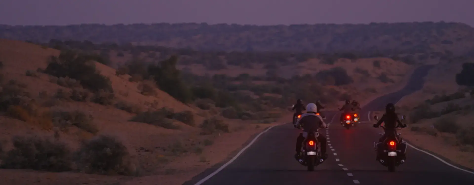 Super meteor 650 Motorcycles ride along a winding road through a desert landscape at dusk.